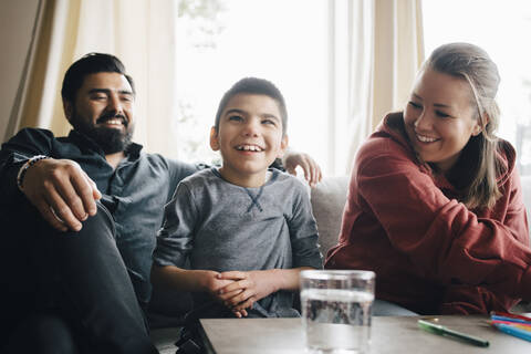 Lächelnde Eltern sehen ihren autistischen Sohn an, während sie auf dem Sofa im Wohnzimmer sitzen, lizenzfreies Stockfoto