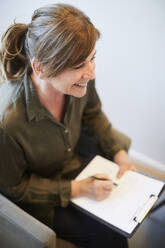 High angle view of smiling therapist writing on clipboard during session - MASF13933