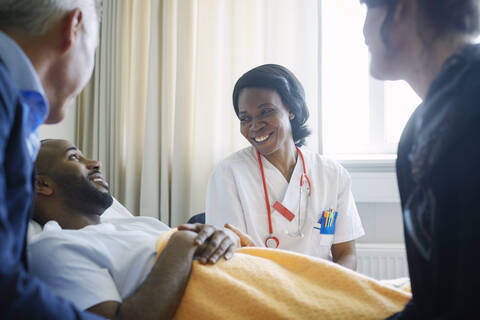 Lächelnde Ärztin im Gespräch mit Patient und Familie auf der Krankenstation, lizenzfreies Stockfoto
