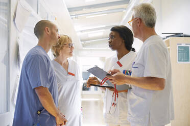 Male and female doctors discussing over digital tablet while standing in corridor at hospital - MASF13977