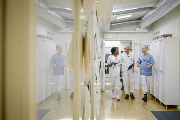 Medizinisches Team diskutiert in voller Länge, während sie gemeinsam durch einen Korridor im Krankenhaus gehen - MASF13980
