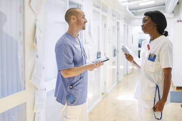 Multiethnisches Gesundheitspersonal diskutiert in einem beleuchteten Korridor im Krankenhaus - MASF13987
