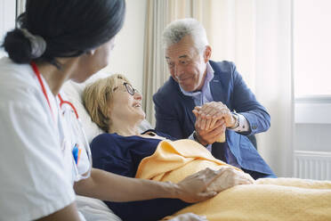 Senior man consoling female patient by doctor in hospital ward - MASF13998