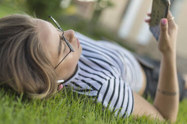 Junge Frau benutzt Smartphone im Gras - FSIF04315