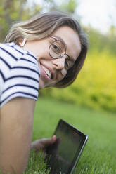 Portrait smiling young woman with digital tablet and headphones in grass - FSIF04331