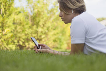 Junge Frau mit Kopfhörern und Smartphone im Gras - FSIF04339