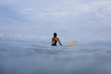 Female surfer straddling surfboard in ocean - FSIF04344