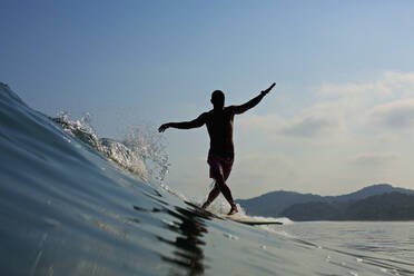 Männlicher Surfer balanciert auf einem Surfbrett und reitet auf einer Welle - FSIF04347