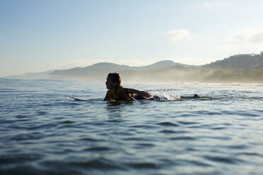 Silhouette boy surfer paddling out on sunny ocean, Sayulita, Nayarit, Mexico - FSIF04365