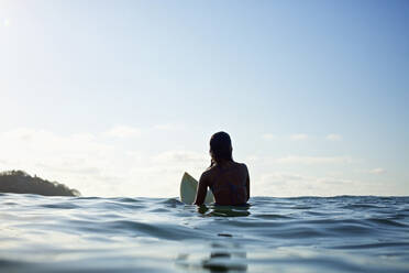 Silhouette female surfer straddling surfboard, waiting in sunny blue ocean - FSIF04366