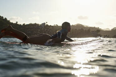 Silhouette female surfer paddling out on sunny, sunset ocean - FSIF04367