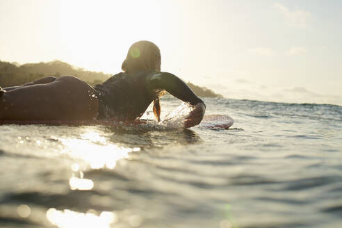 Weibliche Surferin paddelt auf dem sonnigen Meer bei Sonnenuntergang - FSIF04368