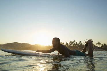 Männlicher Surfer paddelt bei Sonnenuntergang auf dem Meer, Sayulita, Nayarit, Mexiko - FSIF04376