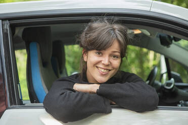 Porträt einer lächelnden jungen Frau, die sich aus dem Autofenster lehnt - FSIF04401