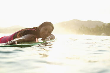 Porträt einer selbstbewussten, gelassenen Surferin, die auf einem Surfbrett im sonnigen Meer liegt - FSIF04410