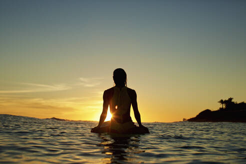 Silhouette einer Surferin, die auf dem Surfbrett auf den Sonnenuntergang am Meer wartet, Sayulita, Nayarit, Mexiko - FSIF04415