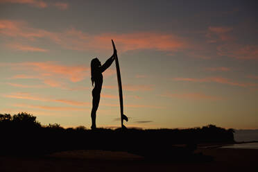 Silhouette female surfer with surfboard on beach at dusk - FSIF04416