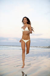 Woman in bikini running in wet sand on beach - FSIF04419