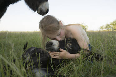 Mädchen umarmt und küsst Baby Esel im Gras - FSIF04428