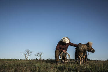 Männlicher Cowboy mit Pony in einem sonnigen ländlichen Feld - FSIF04433