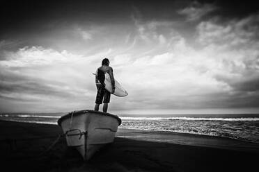 Männlicher Surfer mit Surfbrett auf einem gestrandeten Boot, Higuera Blanca, Nayarit, Mexiko - FSIF04436