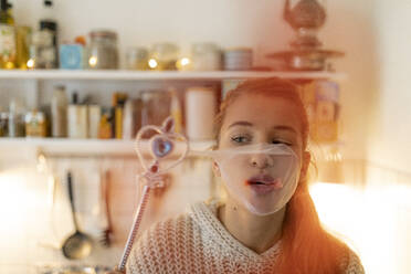 Junge Frau in der Küche zu Hause mit Zauberstab und geplatzter Kaugummiblase - GUSF02473
