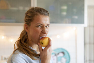 Porträt einer jungen Frau, die zu Hause einen Apfel isst - GUSF02477