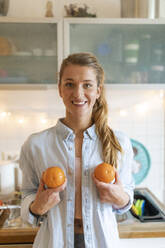 Portrait of happy young woman holding oranges at home - GUSF02483