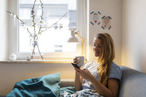Junge Frau benutzt Handy auf der Couch zu Hause, lizenzfreies Stockfoto