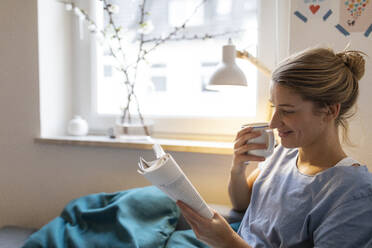 Young woman reading book on couch at home - GUSF02490