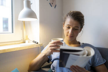 Junge Frau liest ein Buch auf der Couch zu Hause - GUSF02491