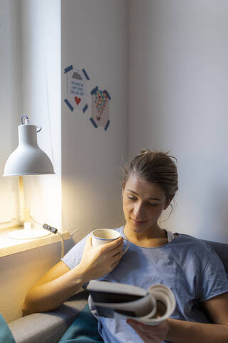 Young woman reading book on couch at home stock photo