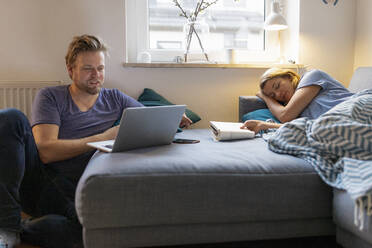 Junge Frau, die mit ihrem Partner zu Hause auf der Couch liegt und einen Laptop benutzt - GUSF02495