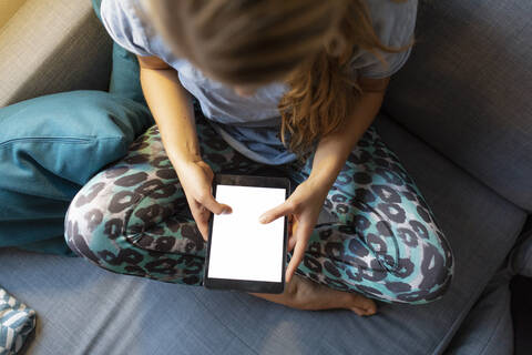 Draufsicht auf eine junge Frau, die zu Hause auf der Couch sitzt und ein Tablet benutzt, lizenzfreies Stockfoto