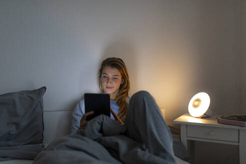 Junge Frau liegt nachts zu Hause im Bett und benutzt ein Tablet - GUSF02509