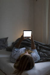 Junge Frau liegt nachts zu Hause im Bett und benutzt ein Tablet - GUSF02511