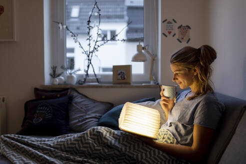 Young woman reading illuminated book on couch at home - GUSF02529