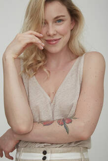 Portrait of smiling blond woman with tattoo on forearm - PGCF00005