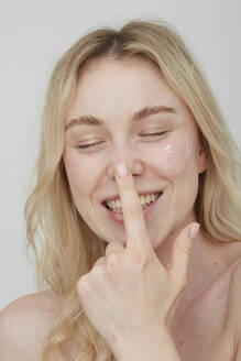 Portrait of laughing young woman applying cream on her face - PGCF00020