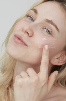 Portrait of young woman applying cream on her face - PGCF00021