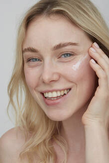 Portrait of smiling young woman applying cream on her face - PGCF00022