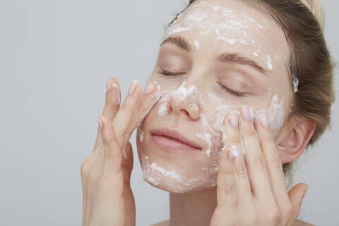 Portrait of blond young woman with eyes closed applying cream on her face stock photo