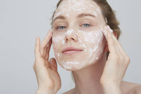 Portrait of blond young woman applying cream on her face - PGCF00030