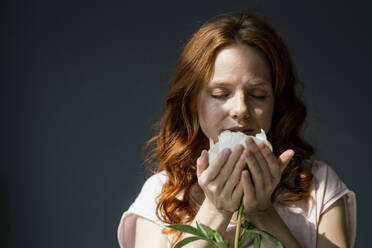 Portrait of redheaded woman smelling white peony - KNSF06496