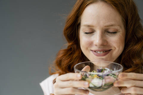 Porträt einer lächelnden rothaarigen Frau, die an Blüten in einer Glasschale riecht, lizenzfreies Stockfoto