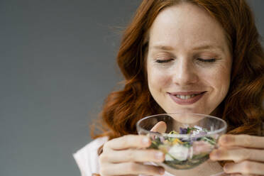 Porträt einer lächelnden rothaarigen Frau, die an Blüten in einer Glasschale riecht - KNSF06501