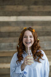 Portrait of laughing redheaded woman with blossoms in hair drinking lemonade - KNSF06516