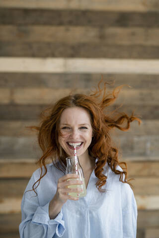 Porträt einer lachenden rothaarigen Frau mit wehendem Haar, die Limonade trinkt, lizenzfreies Stockfoto