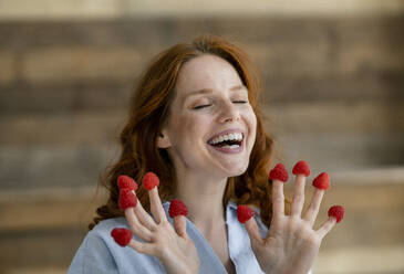 Porträt einer lachenden rothaarigen Frau mit Himbeeren an den Fingerspitzen - KNSF06524