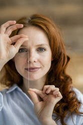 Portrait of redheaded woman holding thread of dental floss - KNSF06531